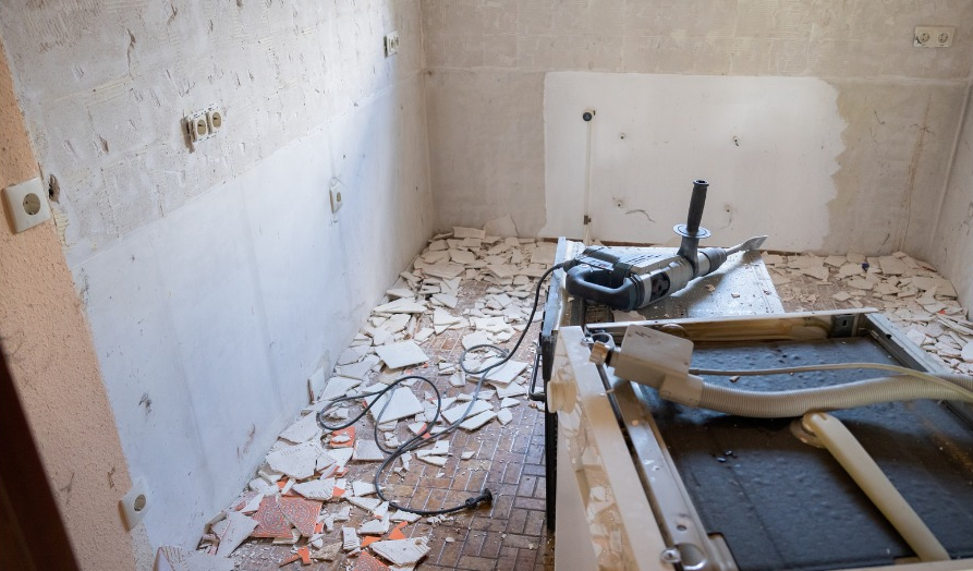 A room with a lot of broken tiles and a drill on the floor.