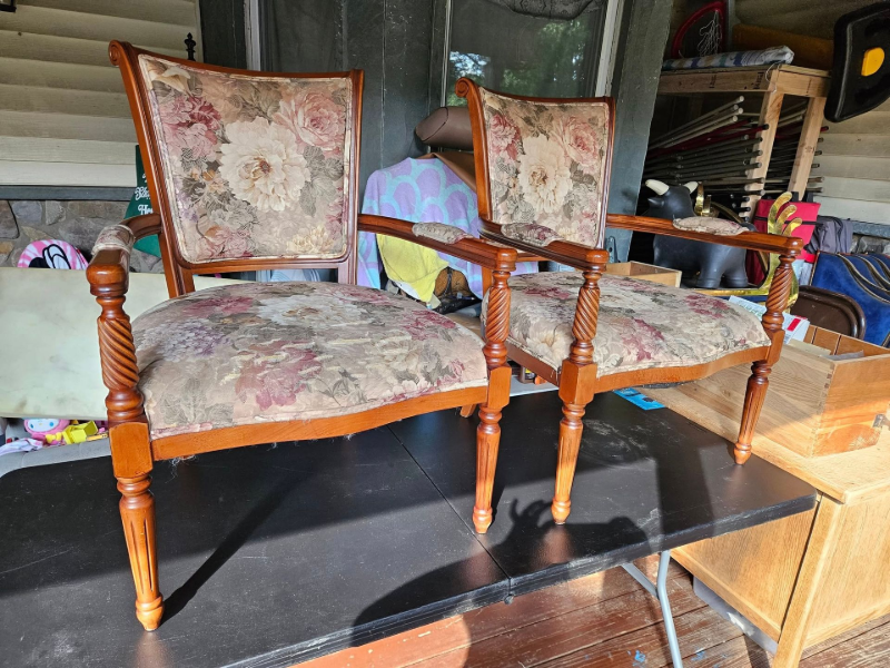 Two floral-upholstered wooden armchairs on a black platform in a storage area.