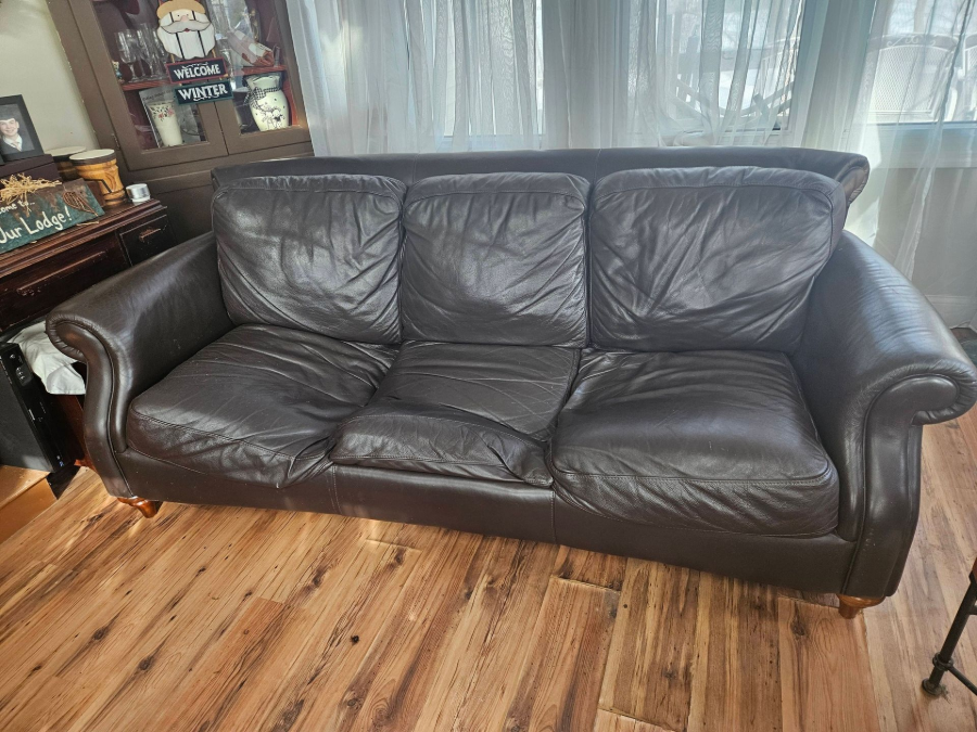 Black leather sofa in a living room with wood flooring and sheer curtains behind it