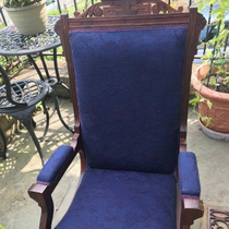 Blue upholstered wooden armchair on a patio with potted plants nearby