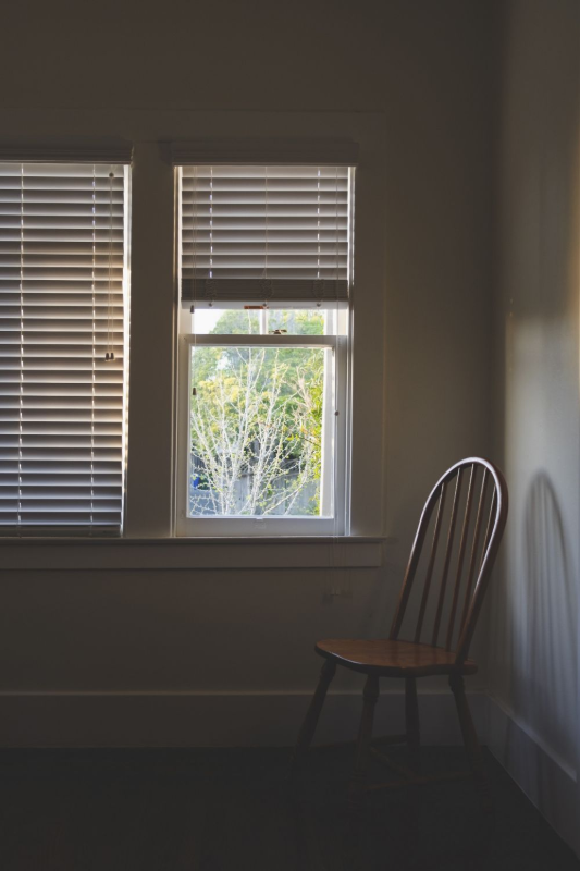 Dim room with a wooden chair by a window with blinds and daylight outside