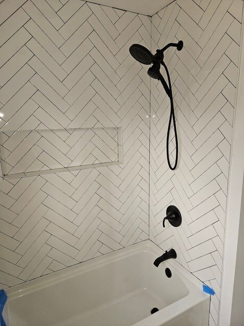 A bathroom with white tiles and a black shower head.