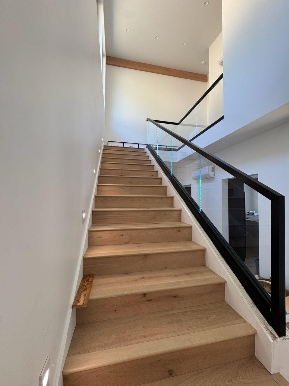 A wooden staircase with a black railing and a glass railing