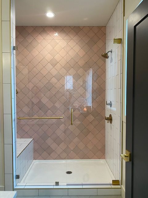 A bathroom with pink tiles and a walk in shower with a glass door.