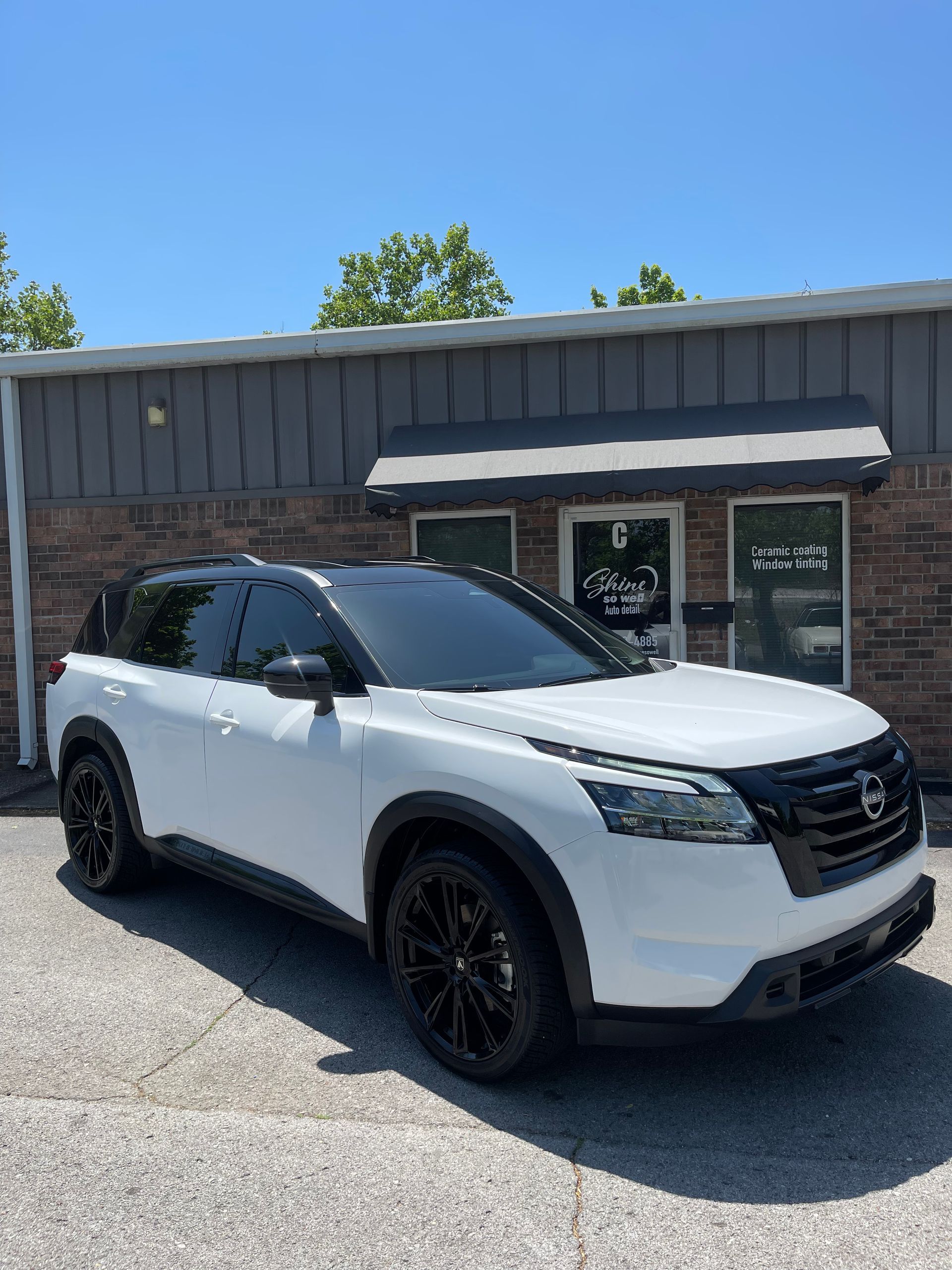 White Nissan Pathfinder SUV with black accents parked in front of a storefront on a sunny day.
