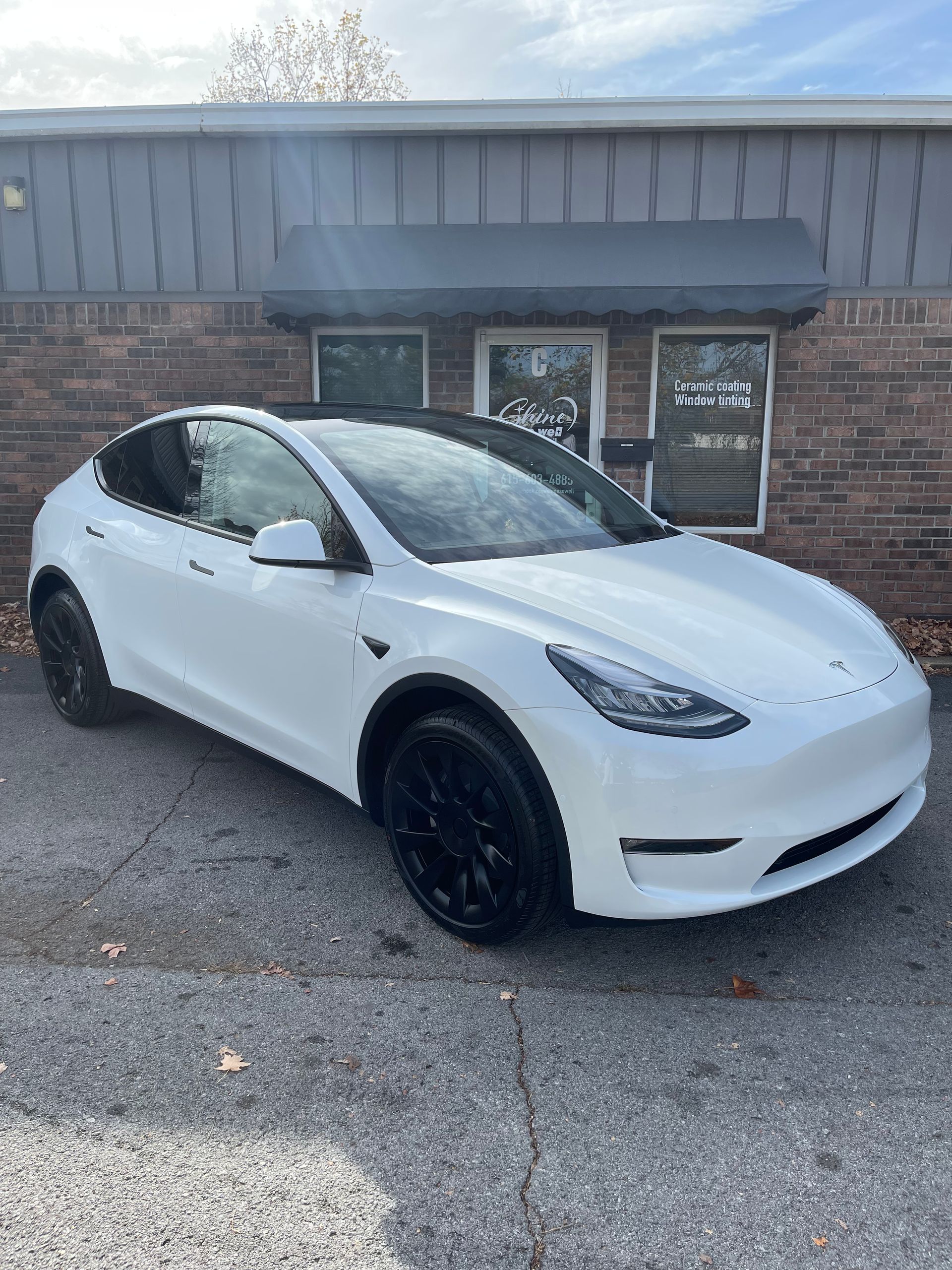 White Tesla Model Y parked in front of a building with a black awning.