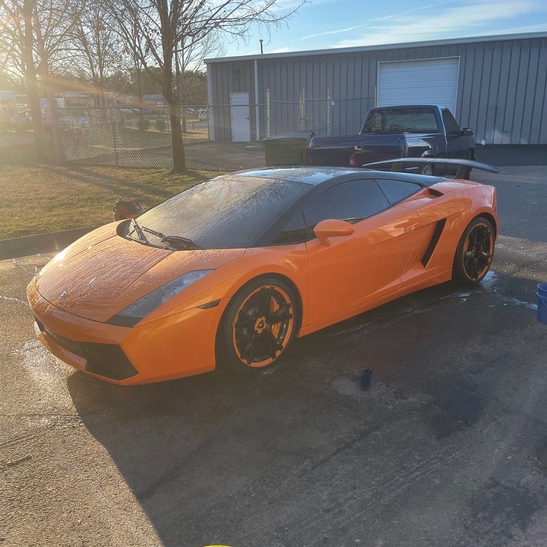 Orange Lamborghini sports car parked outside. Black roof, wheels; sunny day.