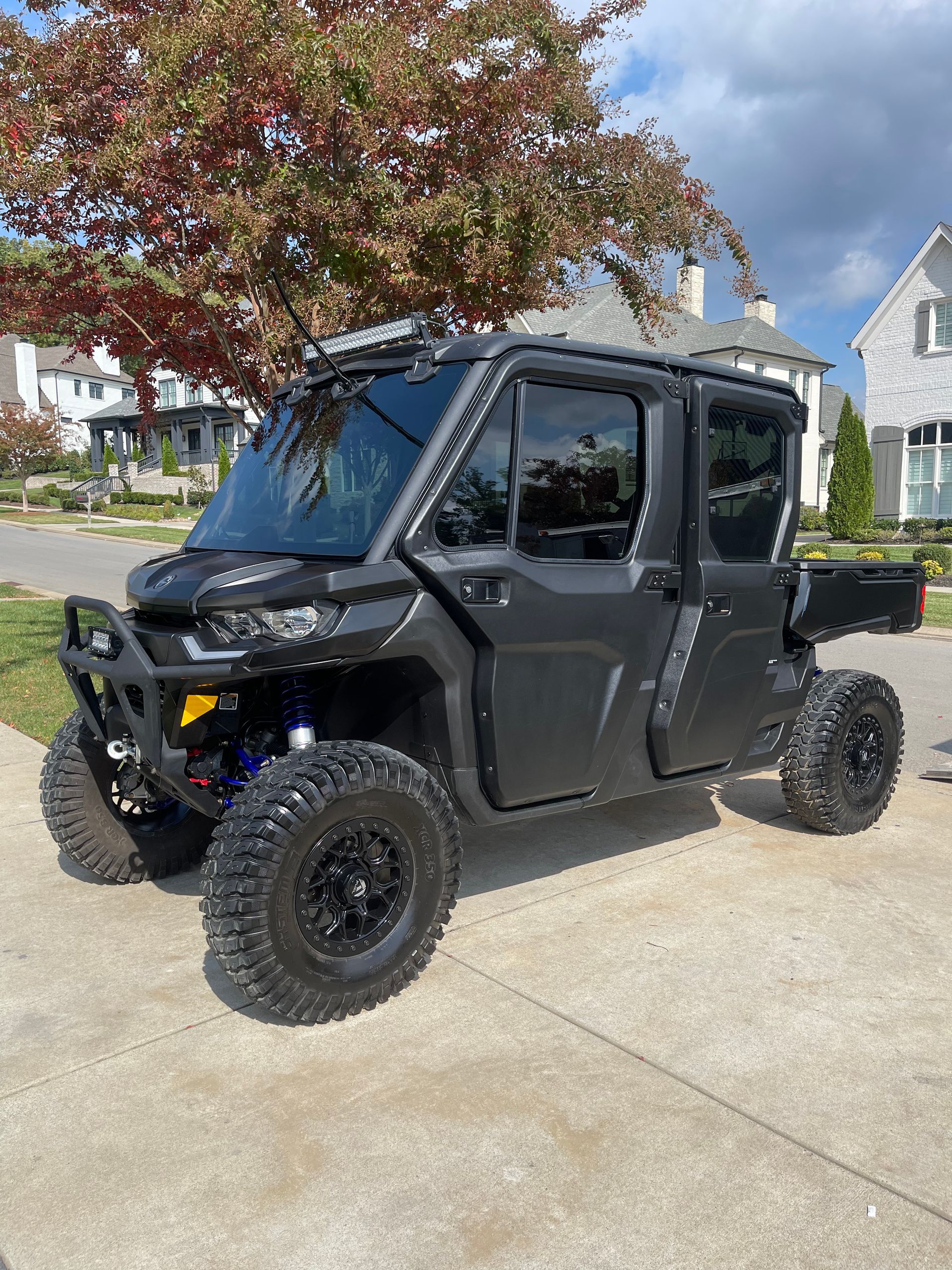 Dark gray off-road utility vehicle parked on a paved driveway with a house and tree in the background.