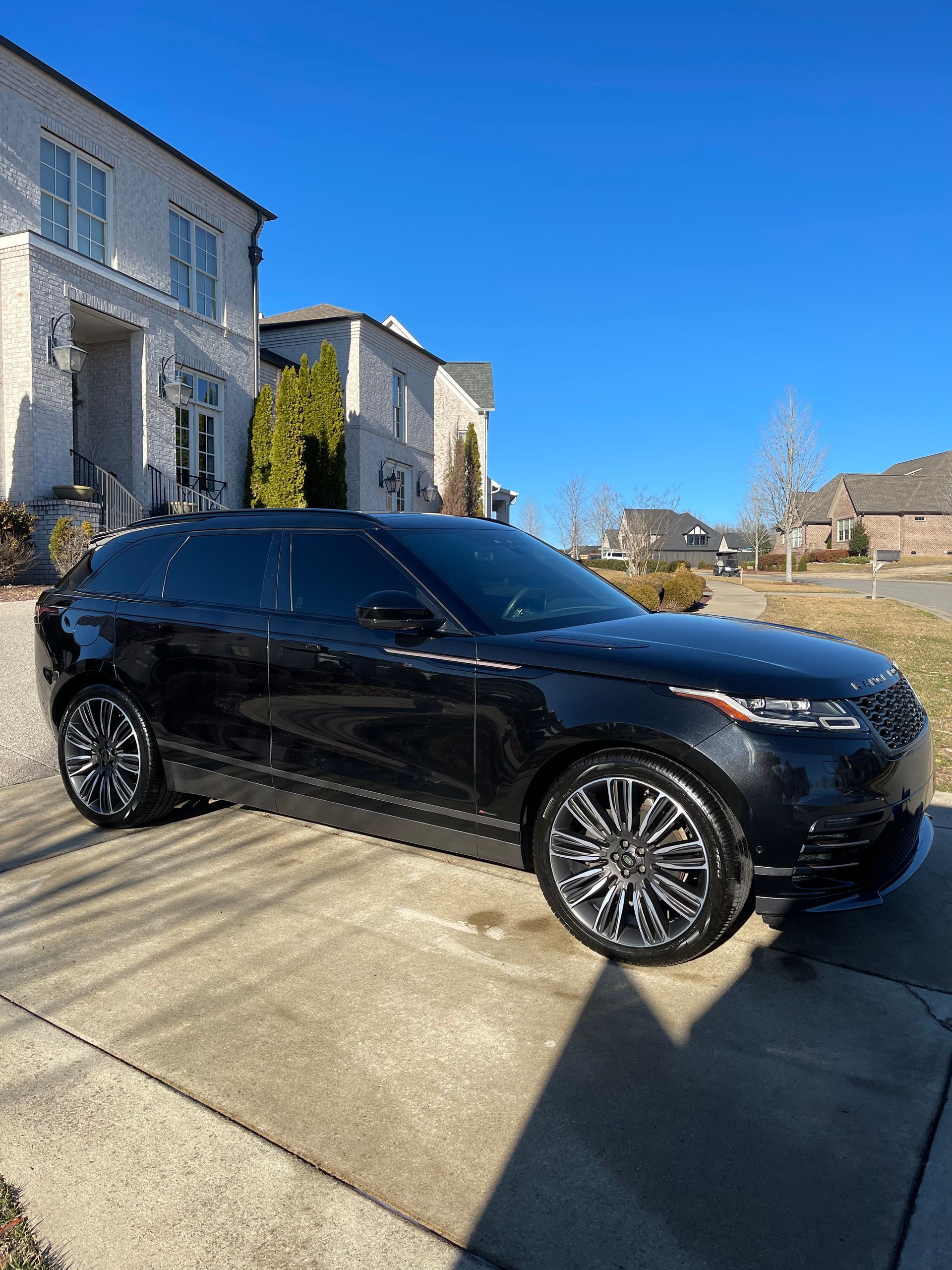 Black Range Rover Velar parked on a driveway in front of a modern house on a sunny day.