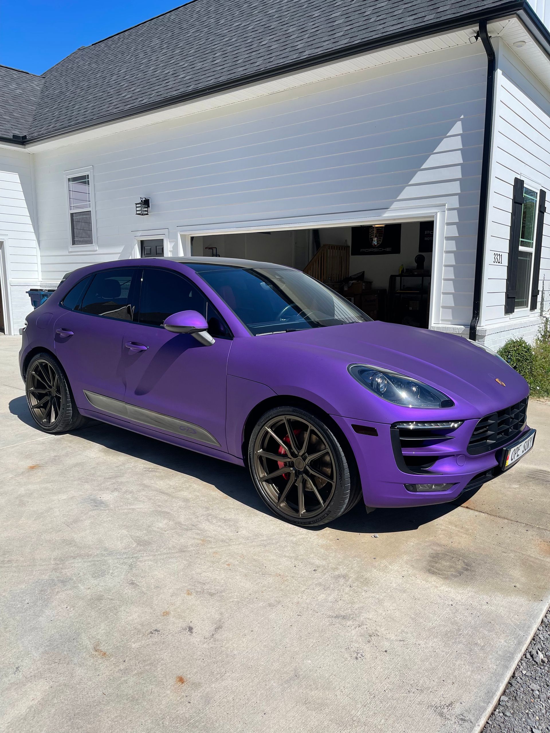 Purple Porsche Macan SUV parked in front of a white house with a garage door.
