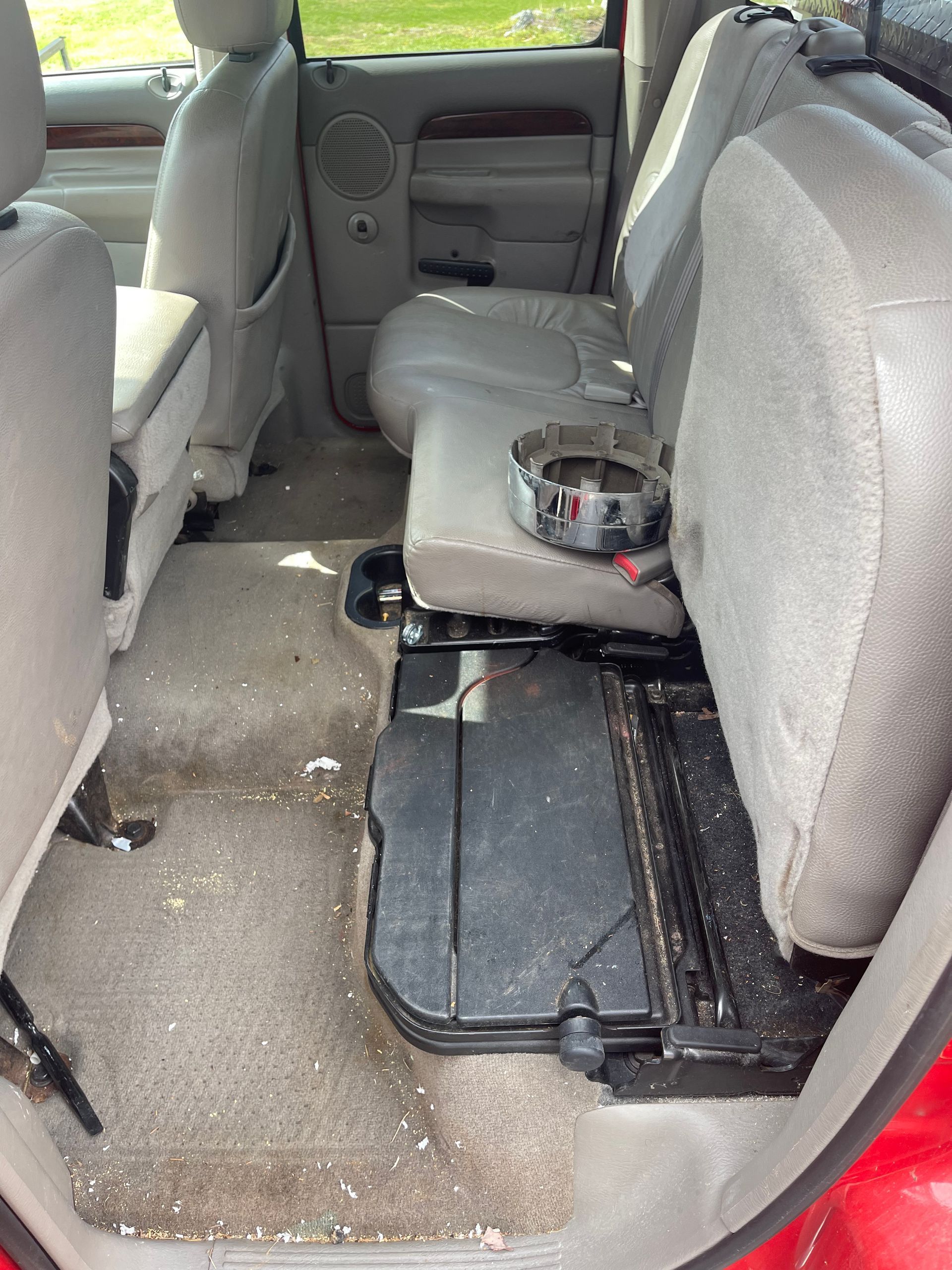 Interior of a red pickup truck's back seat, dirty carpet, light-colored seats, a storage area is exposed.