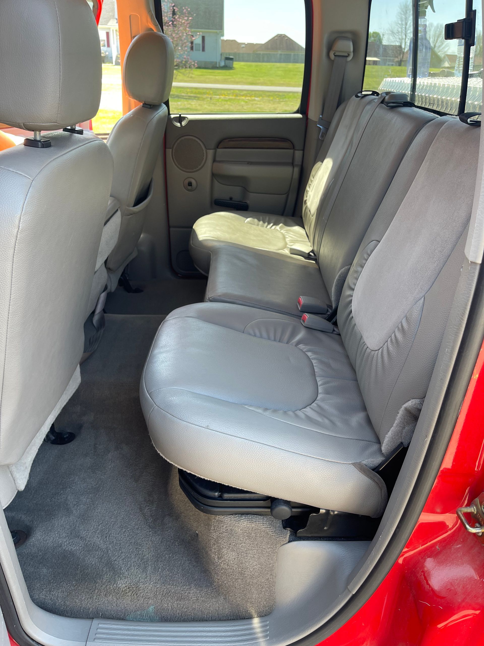 Interior view of a pickup truck's back seat, showing gray leather seats, gray carpet, and a side door.