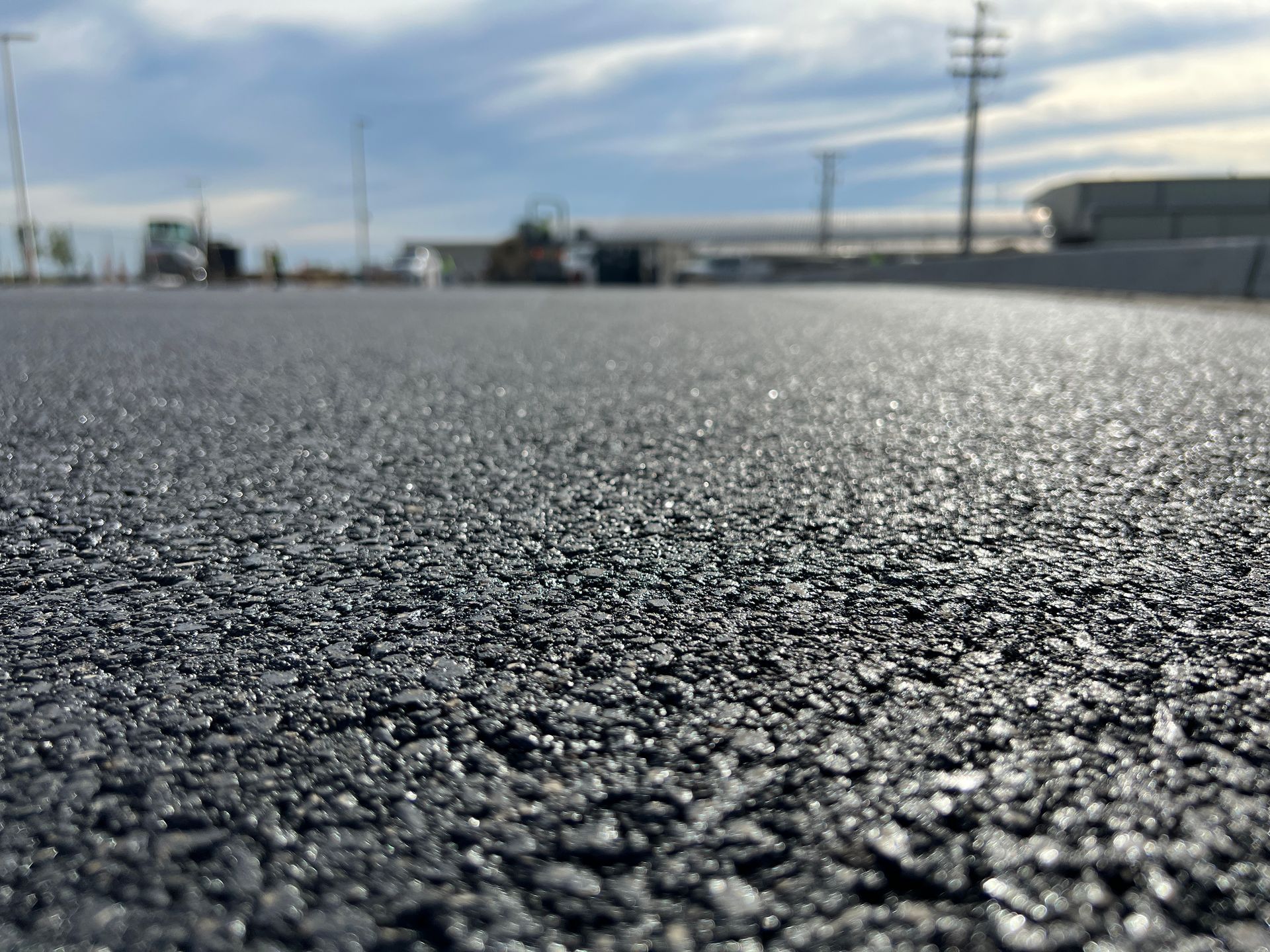 Close-up of freshly paved asphalt surface with blurred background of buildings and sky.