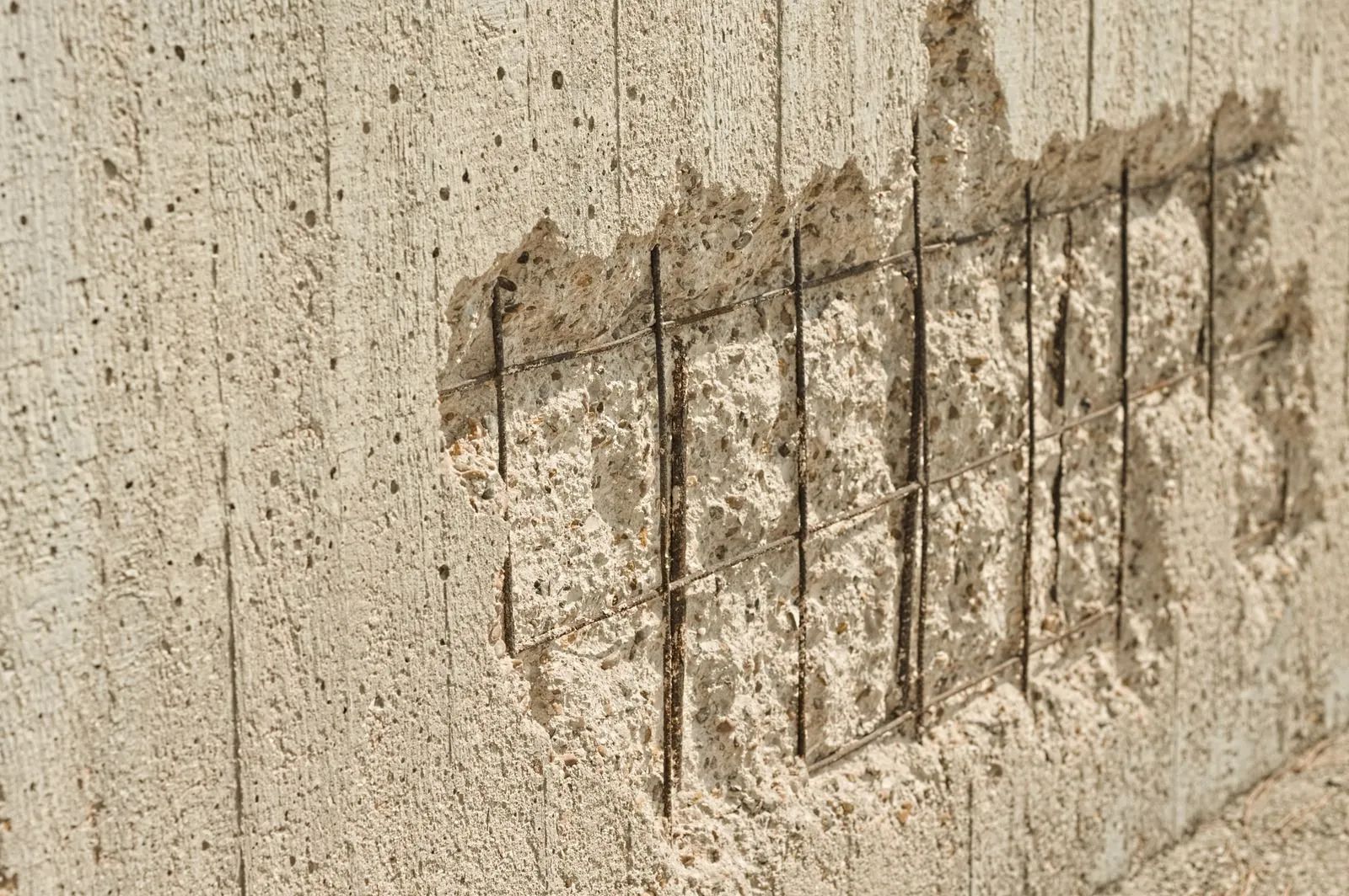 Concrete wall with damaged section exposing reinforcing steel bars.