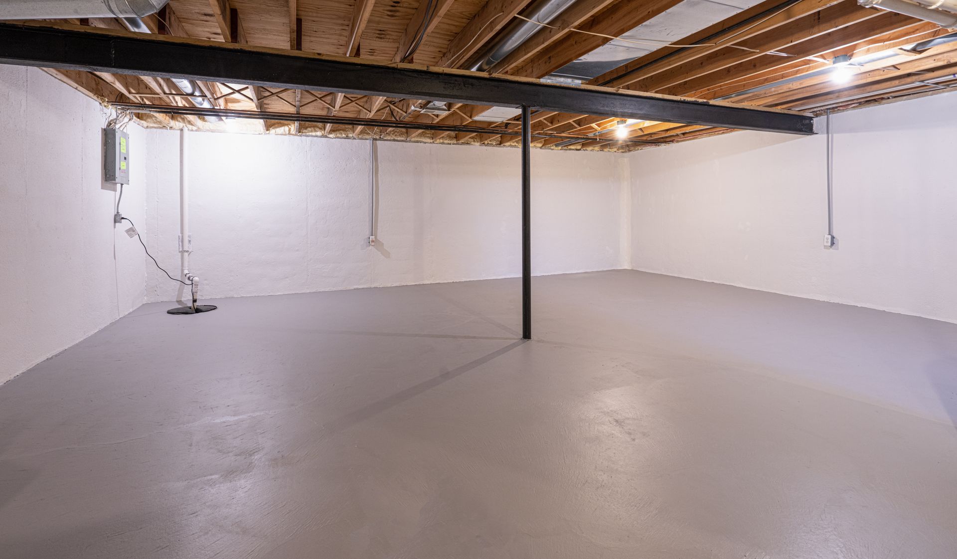 An empty basement with white walls and a wooden ceiling.