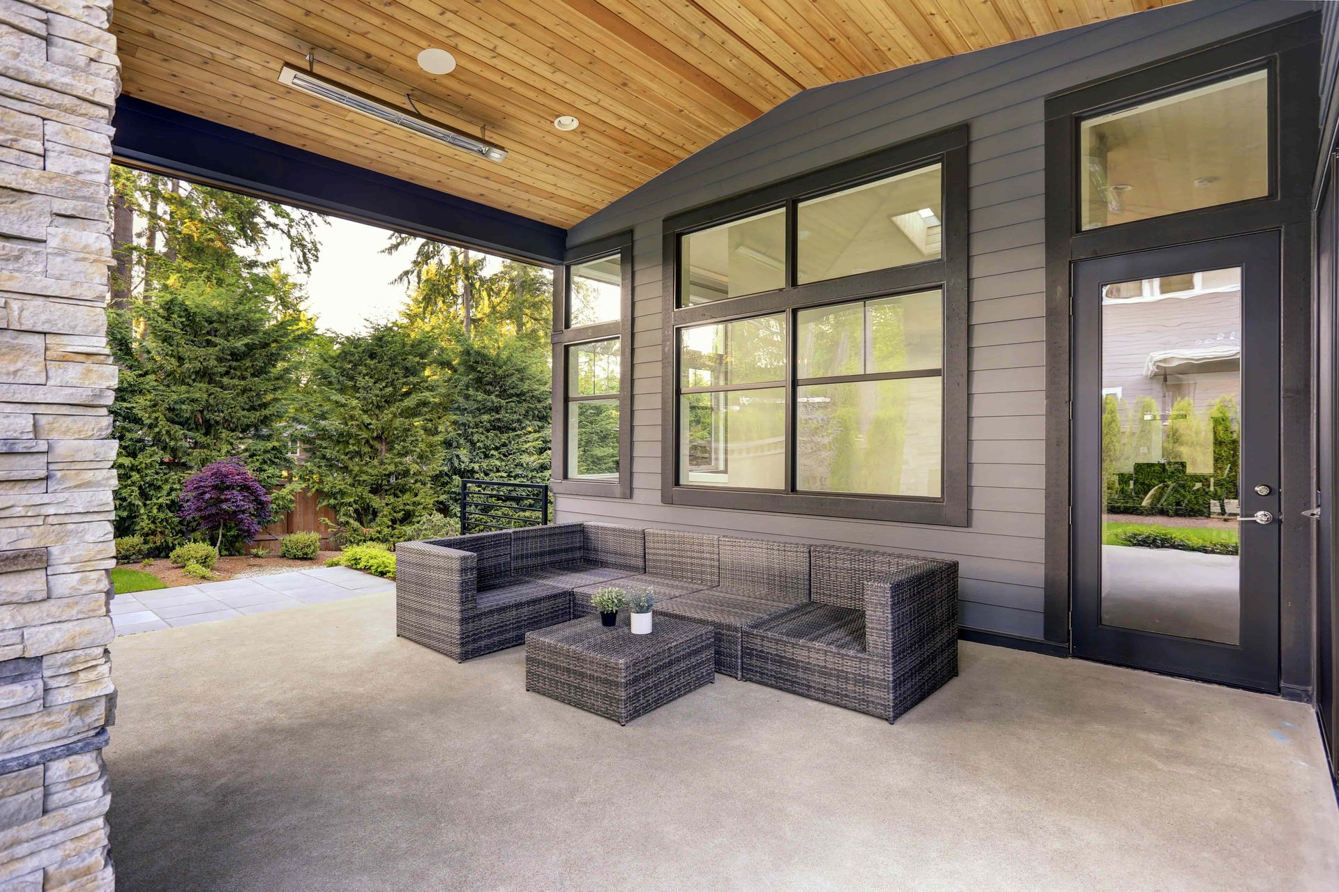 Covered patio with gray sofa, wooden ceiling, gray walls, and view of trees and yard.