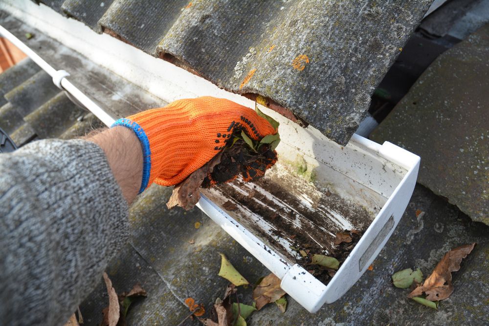 A Person Wearing Orange Gloves is Cleaning a Gutter on a Roof — Gutterpro Townsville In Mt Louisa, QLD