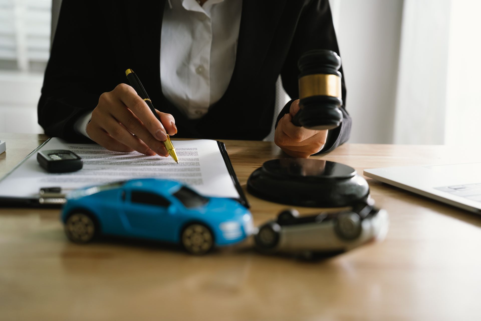 A lawyer uses a gavel near a toy car, symbolizing legal proceedings.