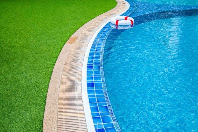 Curved swimming pool edge with blue water, tiled border, and green grass nearby