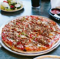 Large pizza on a metal tray with salad and drinks in the background