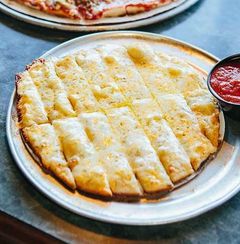 Cheesy baked pizza or flatbread on a metal plate with a cup of marinara sauce