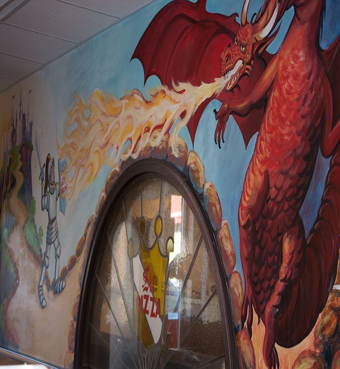 Graffiti mural of a red dragon breathing fire on a wall beside a glass doorway