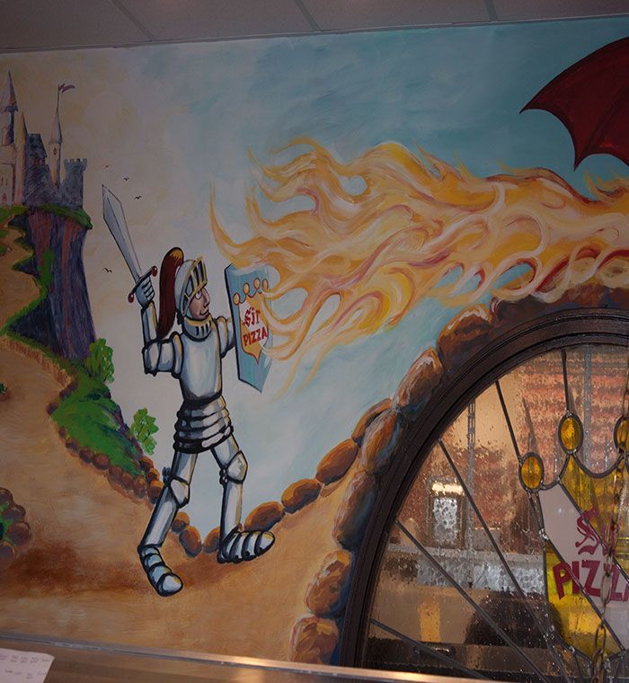 Mural of a knight-like figure holding a cup, with flame-like hair, beside a castle and arched pizza shop window