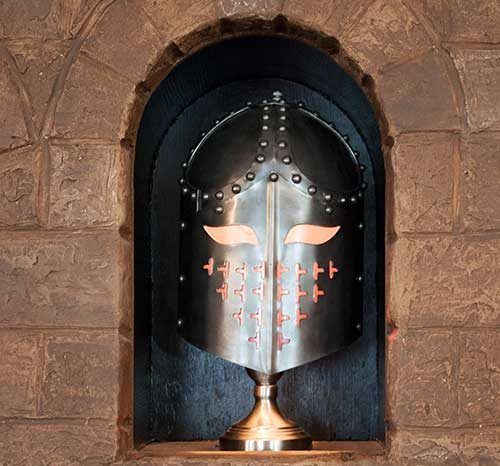 Medieval suit of armor displayed in a stone alcove, with a dark visor and red accents