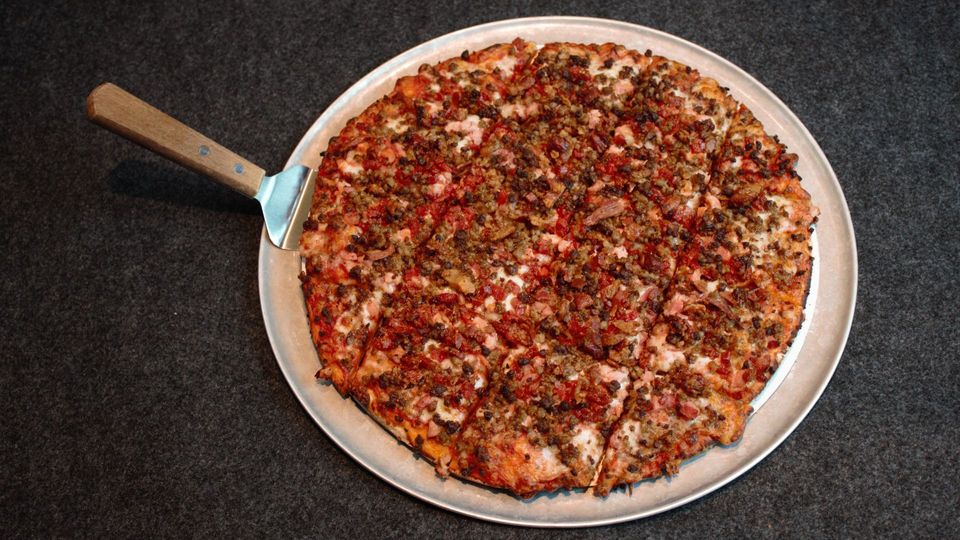 Round pizza on a white plate with a wooden-handled pizza cutter on a dark surface