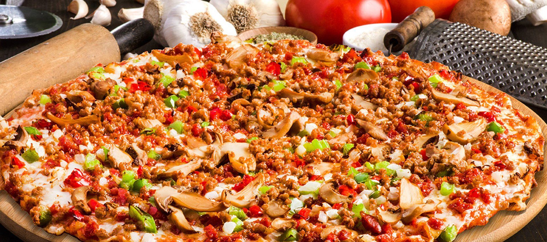 Close-up of a large pizza topped with mushrooms, peppers, and meat on a wooden board