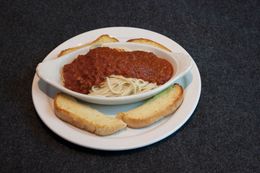 Spaghetti with red sauce in a white bowl, served with two slices of garlic bread on a plate