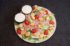Plate of salad with cherry tomatoes and two small bowls of dressing on a dark table