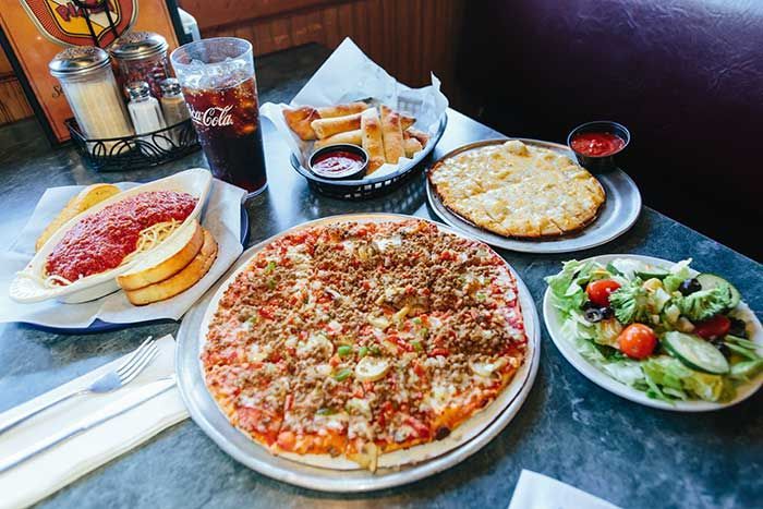 Table with pizza, pasta, salad, fries, and drinks in a restaurant setting