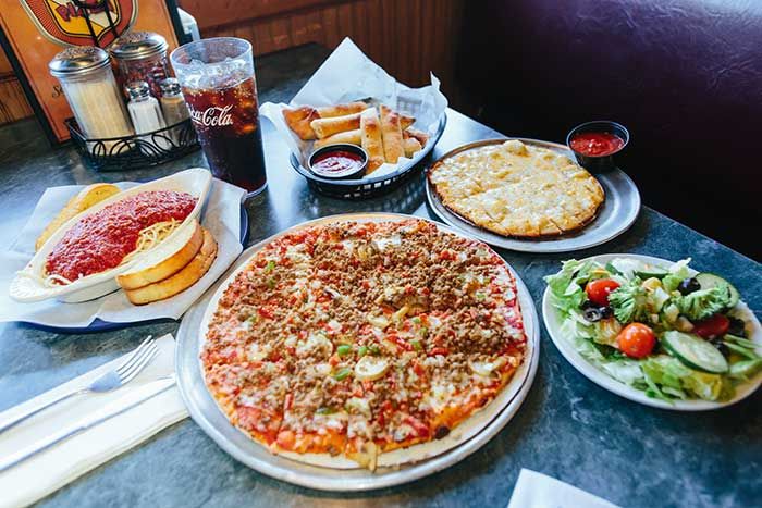 Table with pizza, pasta, salad, fries, and drinks in a restaurant setting