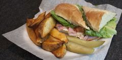Sandwich with lettuce, tomato, and roast potatoes on white paper, on a dark table