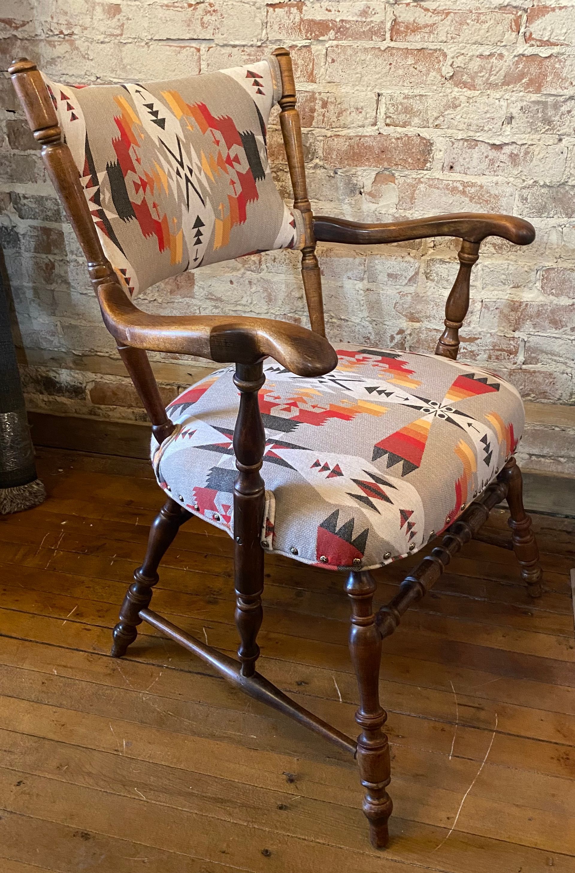 A wooden chair with a patterned seat and back is sitting in front of a brick wall.