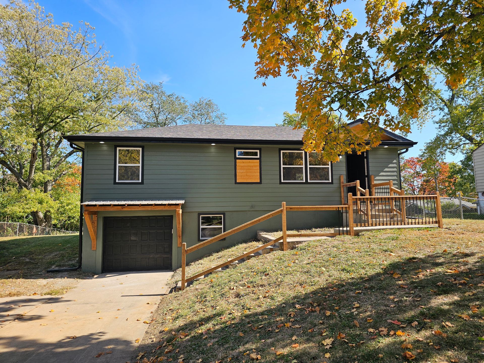 A green house with a garage and a wooden fence in front of it.