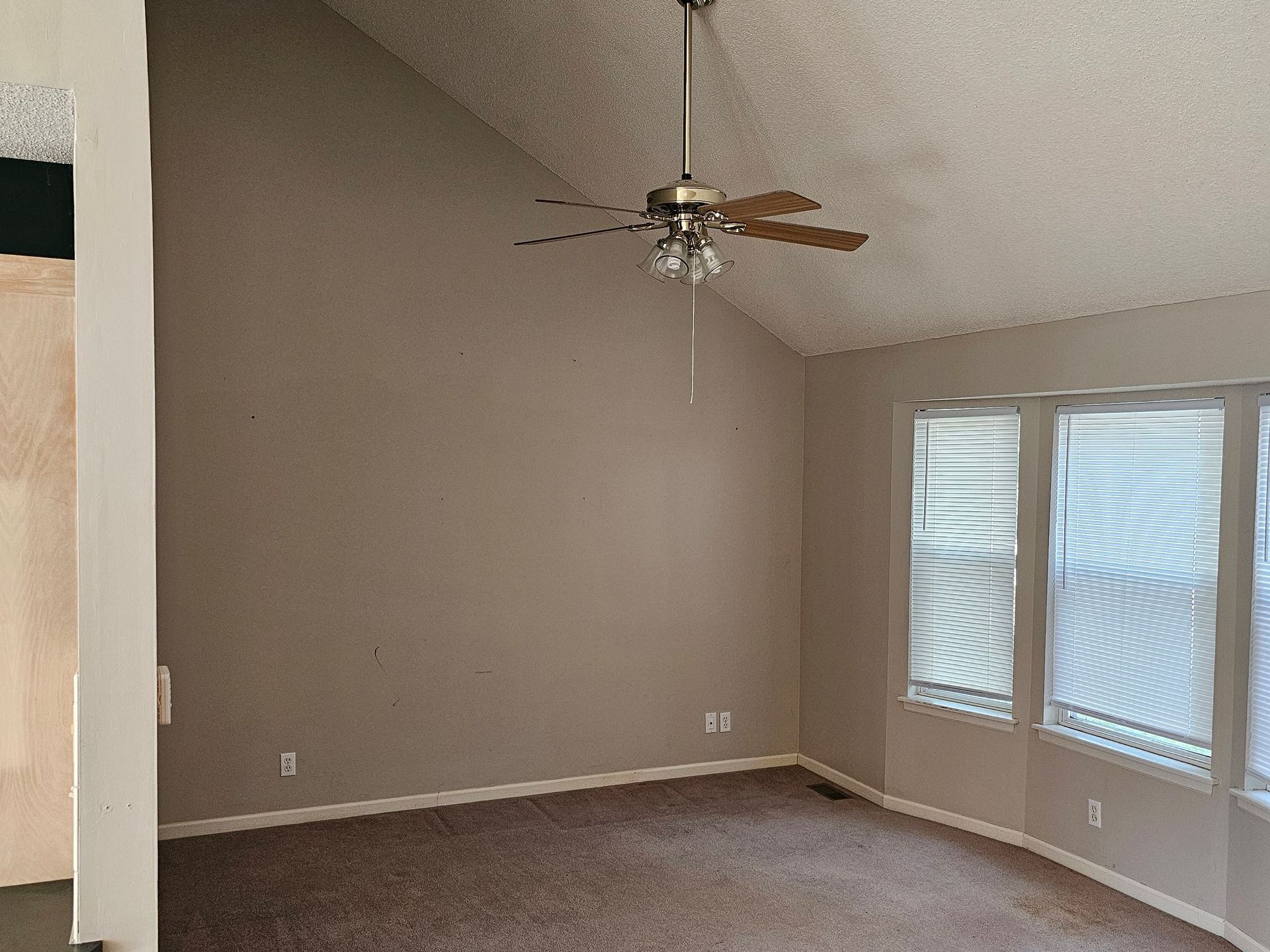 An empty living room with a vaulted ceiling and a ceiling fan.