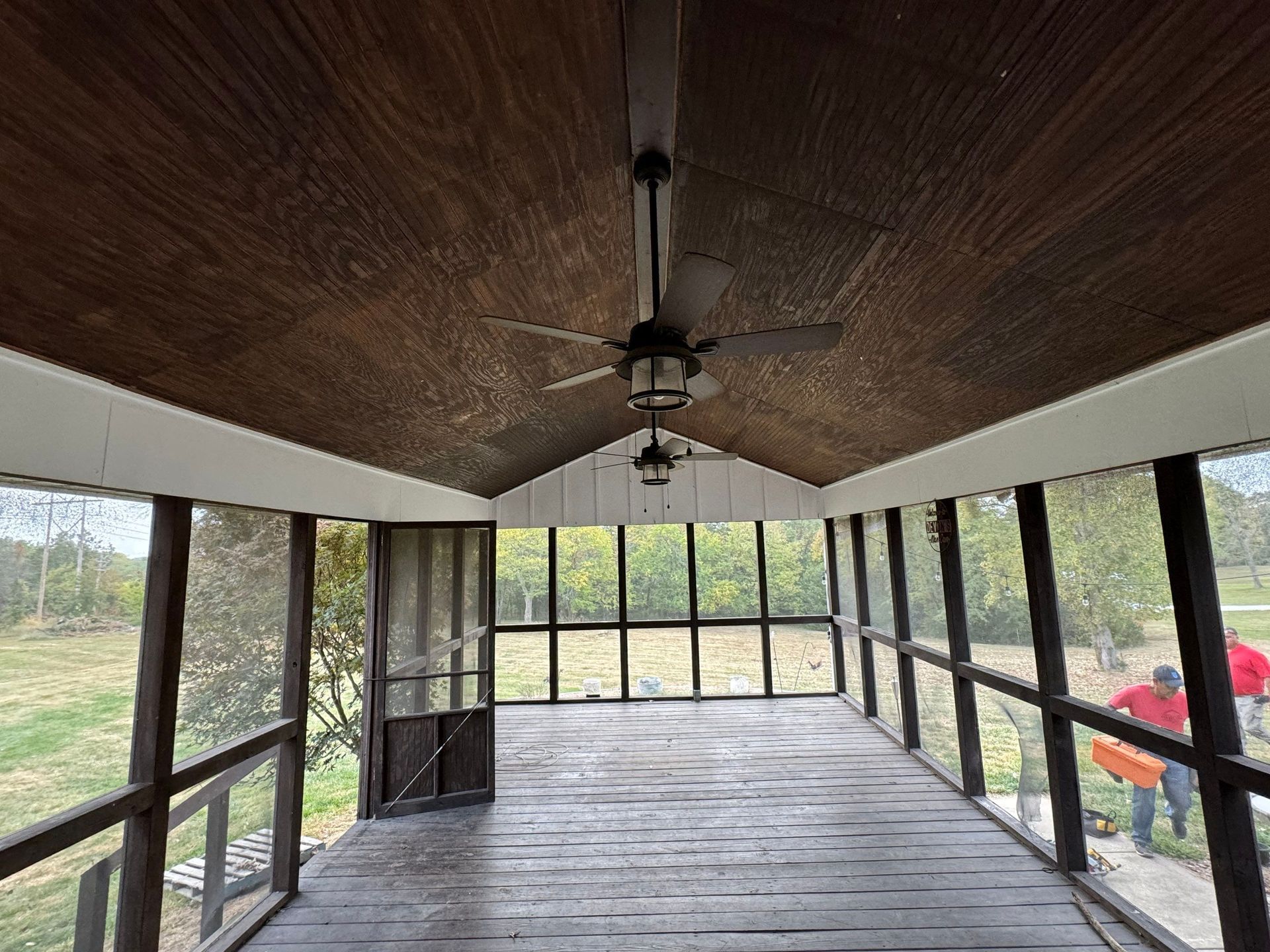 A screened in porch with a ceiling fan and a lot of windows.