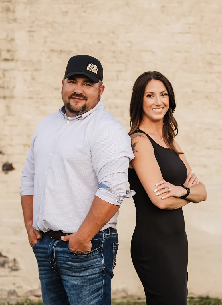 A man and a woman are standing back to back in front of a brick wall.