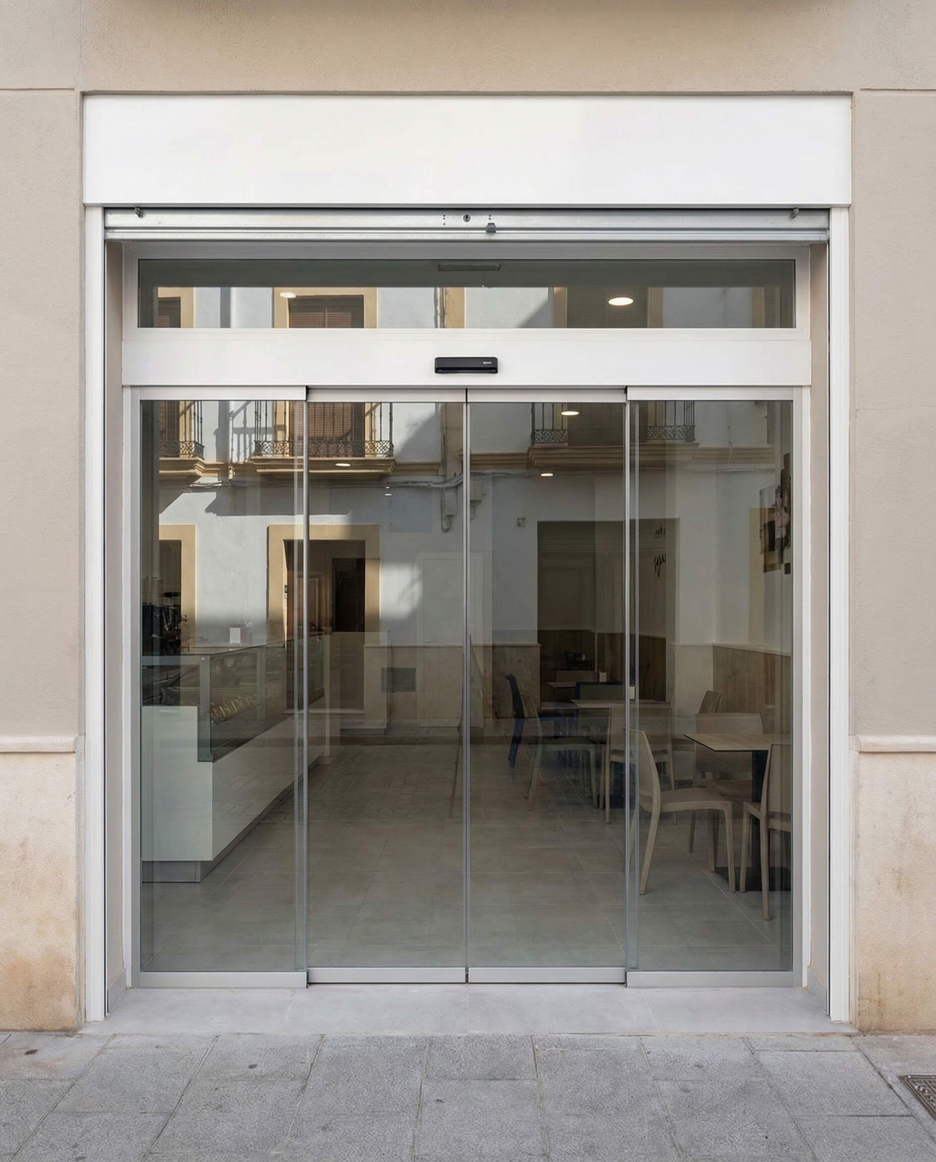Puertas corredizas automáticas de vidrio en la entrada de una tienda. El vidrio reflectante permite ver el interior de la tienda y los edificios circundantes.