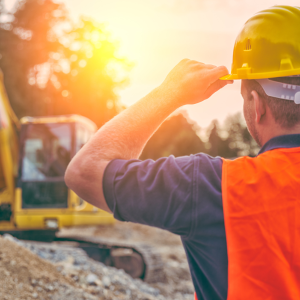 A man wearing a hard hat and an orange vest is looking at a construction site.