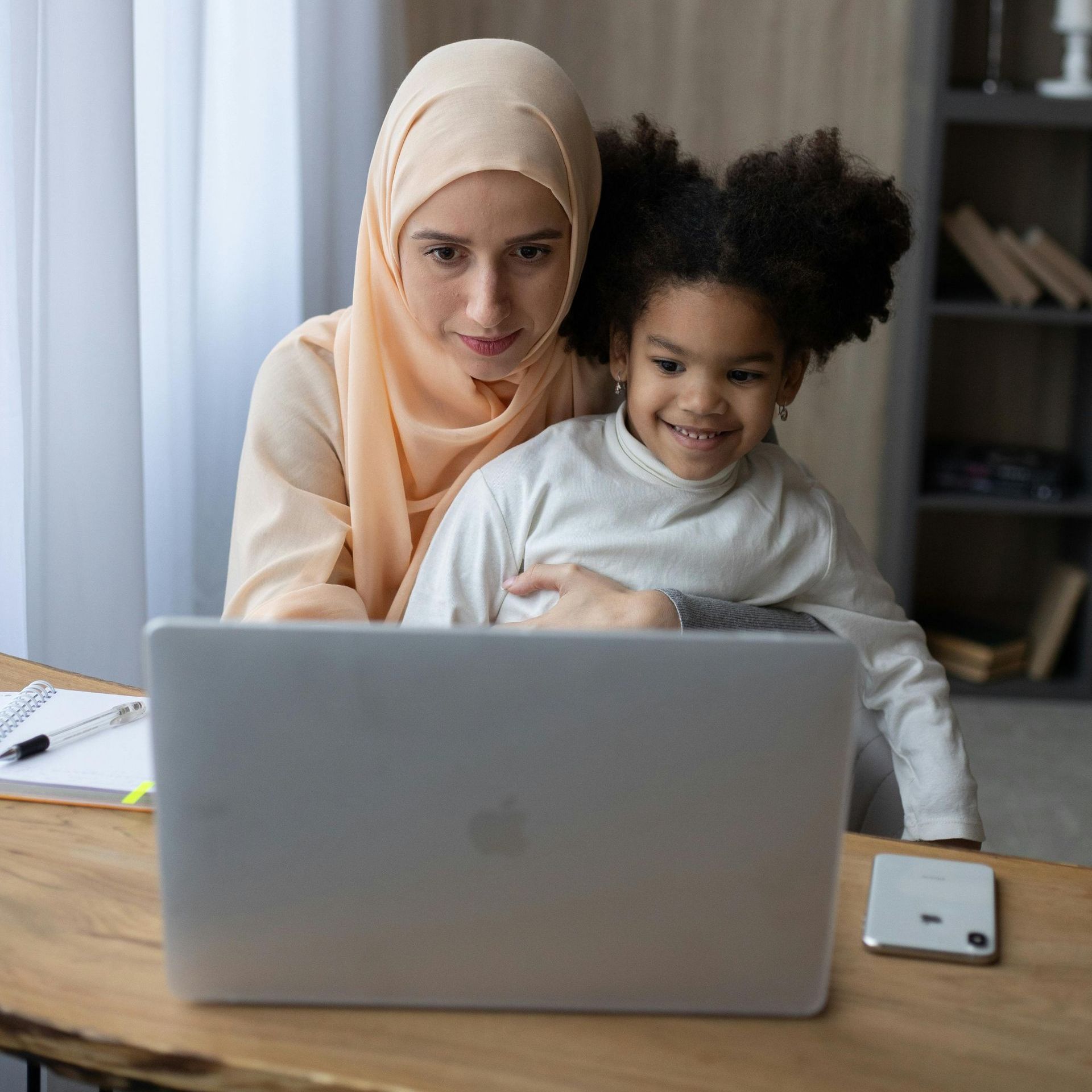 A woman and a child are sitting at a table looking at a laptop.