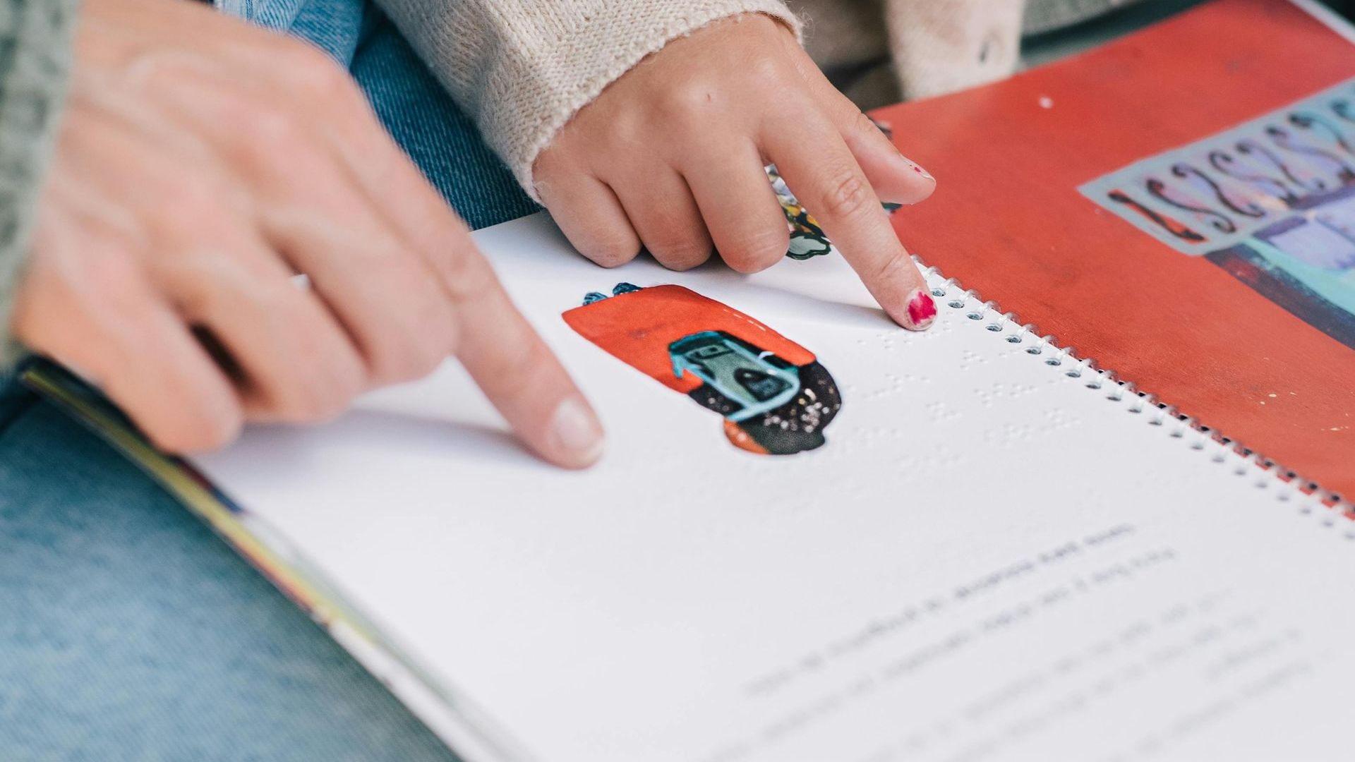 A person is pointing at a picture of a car in a book.