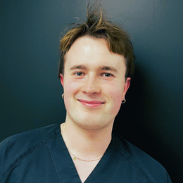 Smilende person med briller og neongrønn skjorte som ser inn i kameraet.