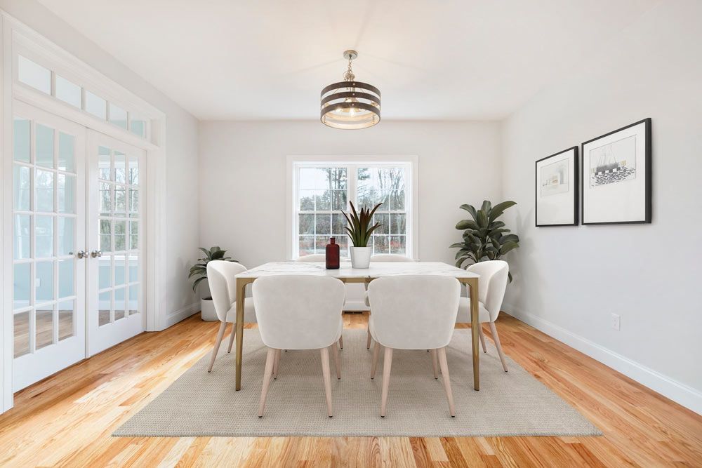 Bright dining room with white chairs, wood floors, large windows, and framed wall art