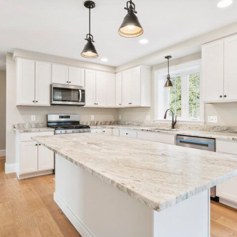 Bright modern white kitchen with large island, stainless appliances, and pendant lights