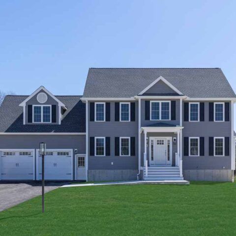 Gray two-story suburban house with white trim, double garage, and manicured green lawn under a clear sky
