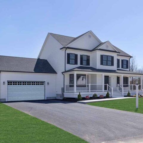 Two-story white suburban house with attached garage, front porch, and driveway under a clear sky
