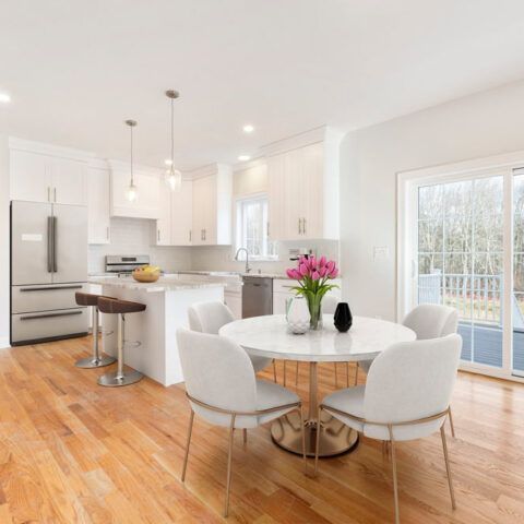 Bright white kitchen and dining area with hardwood floors, round table, and sliding glass doors to a deck